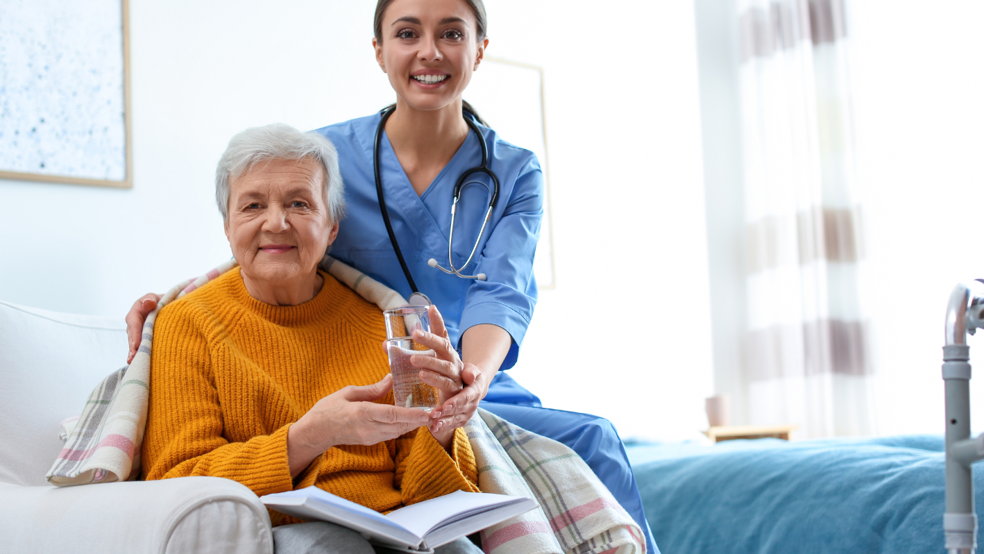 Una enfermera sostiene un vaso de agua junto a una anciana